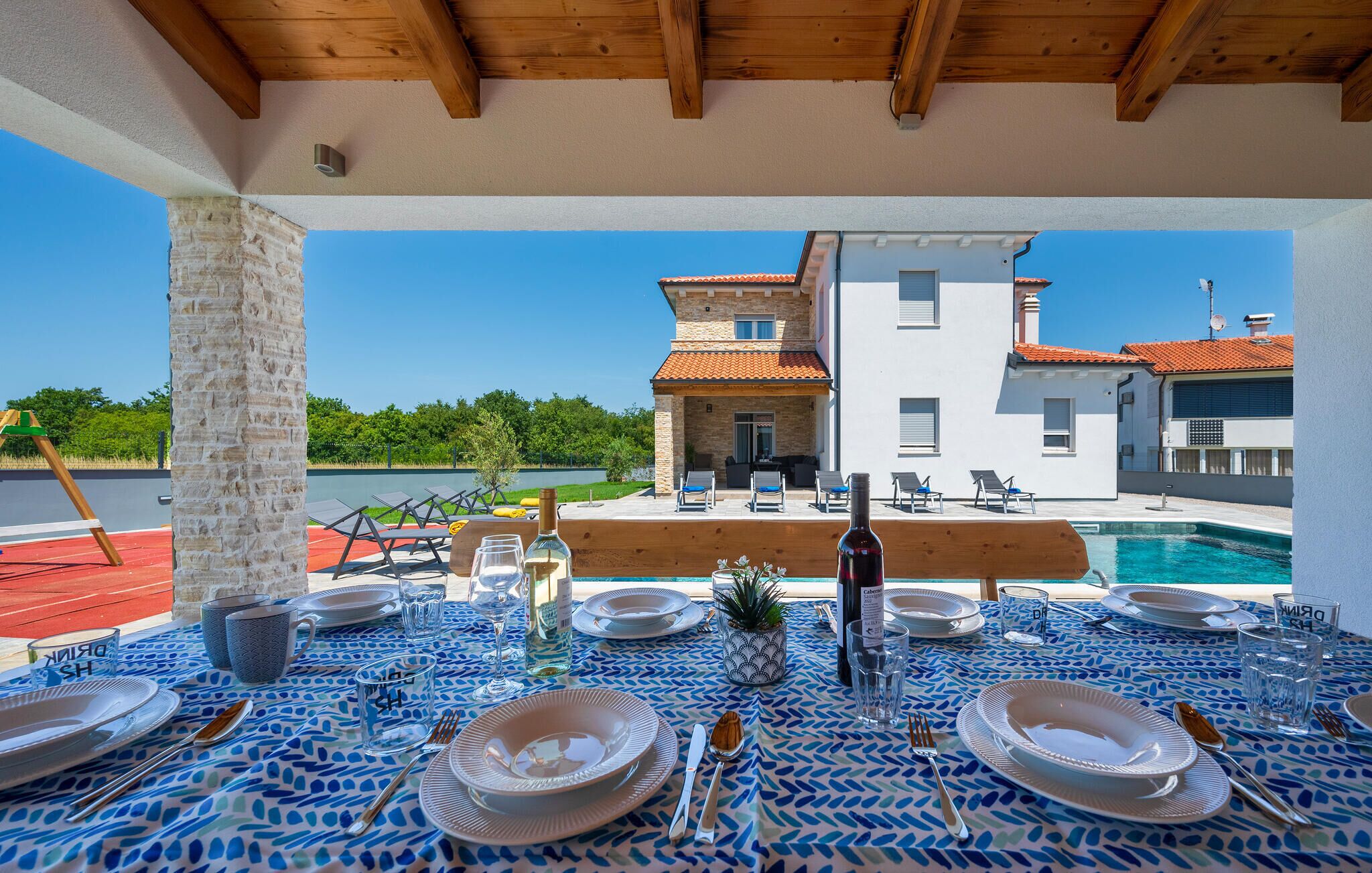 Área de refeições ao ar livre com vista para a piscina, um pilar de pedra e uma mesa posta para quatro pessoas.