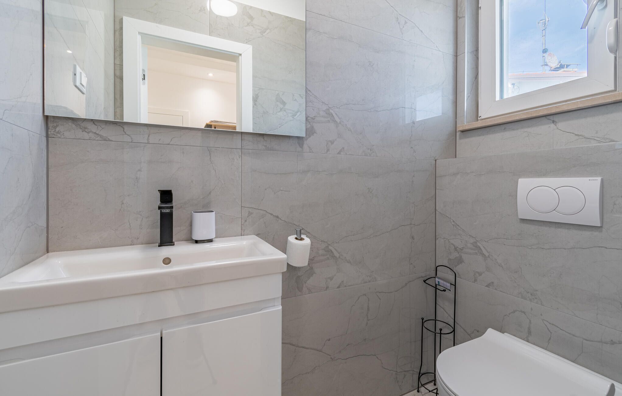 Une salle de bain avec un lavabo blanc, un miroir, un distributeur de serviettes et des toilettes.