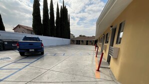 A parking area with a blue truck, a building with multiple windows, and tall trees in the background. - State Motel (South Gate)