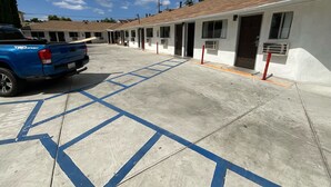 A parking area with marked spaces, a blue pickup truck, and a row of white buildings with brown roofs. - State Motel (South Gate)