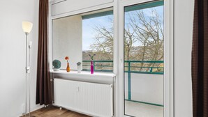 A room with a radiator, a floor lamp, and a window with a view of trees and a building.