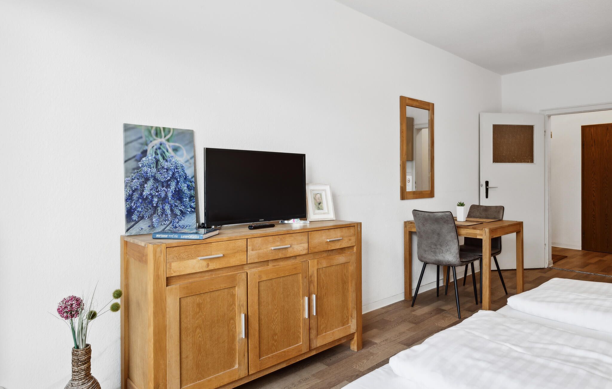 Habitació d'hotel amb un armari de fusta, una televisió, una fotografia emmarcada, una taula petita amb cadires, un mirall i un llit.