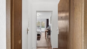 A hallway leading to a bedroom with a bed, a desk, and a chair.