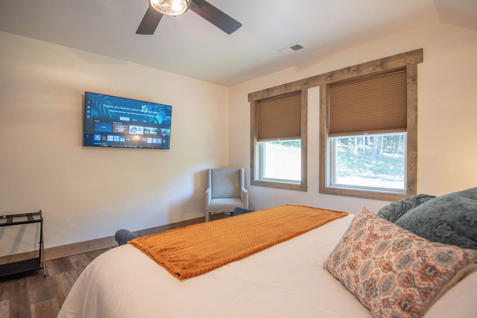 A bedroom with a bed, a chair, a television, and two windows with blinds.