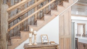 A wooden staircase with a rustic design, a wooden console table with candles and a sign, and a kitchen area in the background.