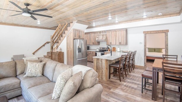 A spacious living area with a sofa, a wooden ceiling, and a kitchen with wooden cabinets and a refrigerator.