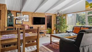 Ett mysigt vardagsrum med träväggar, en matplats med bord och stolar, en soffa och en tv.
