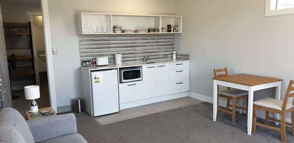 A compact kitchen with white cabinets, a microwave, and a small dining table with chairs.