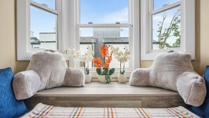 A room with a bench seat, a window with a view of buildings, and a potted plant with flowers.