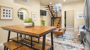 A modern living room with a wooden dining table, a staircase, and a grey sofa.