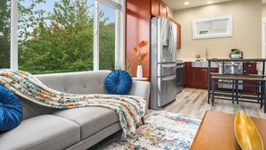 A modern kitchen with a grey sofa, a dining table, and a view of trees outside.