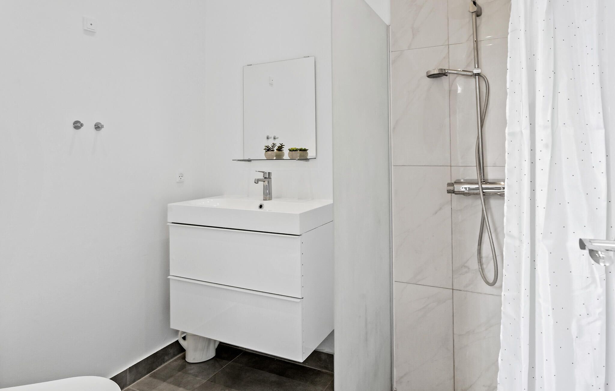 Et moderne badeværelse med et hvidt vaskeskab, et spejl, en bruser og et toilet.
