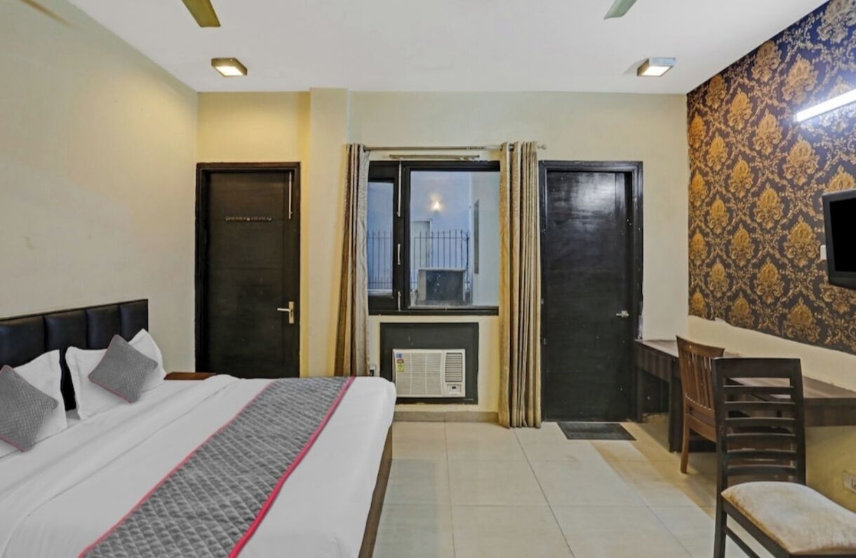 A hotel room with a bed, a desk, a chair, a window with curtains, and a television.