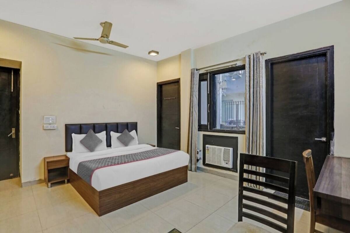 Ein Hotelzimmer mit einem Bett, einem Schreibtisch, einem Sessel, einem Deckenventilator und einem Fenster mit Vorhängen.