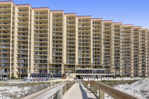 Un hotel de varios pisos con balcones, vistas a la playa y un paseo de madera que conduce a la playa.