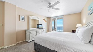 Ein Hotelzimmer mit einem großen Bett, einem Deckenventilator, einem Fernseher und Meerblick durch eine Balkontür.