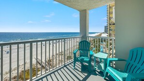 Ein Balkon mit Blick auf Strand und Meer, ausgestattet mit türkisfarbenen Stühlen und einem kleinen Tisch.