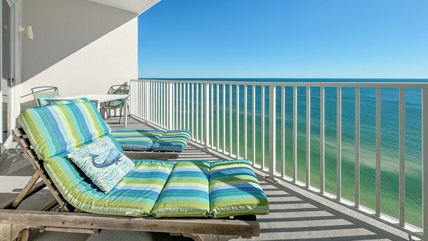 Un balcón con dos sillones de relax, cada uno con cojines a rayas, que da a un mar azul y transparente.