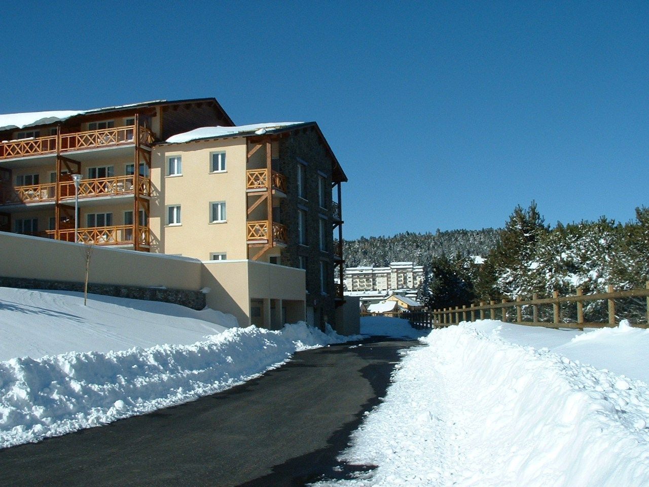 Una carretera cubierta de nieve que lleva a un edificio de varios pisos con balcones.