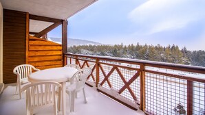 A wooden deck with a table and chairs, overlooking a snowy landscape with trees.