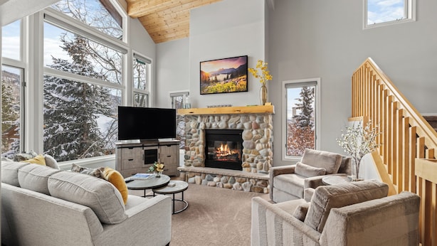 A cozy living room with a stone fireplace, a large flat-screen TV, and comfortable seating. - High Expectations! AC, Community Pool and Spa, Close to Base, New Furnishings! (Steamboat Springs)