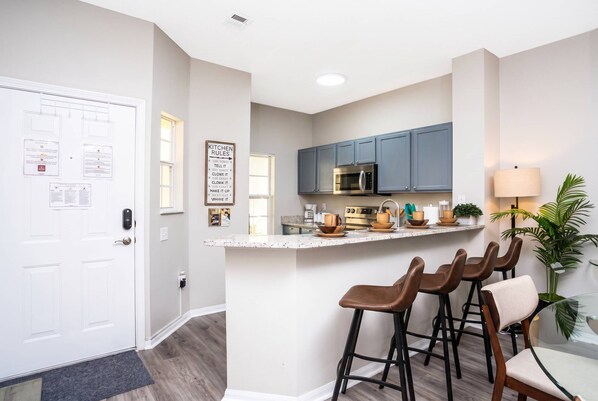 A modern kitchen with a bar area, bar stools, and a countertop with various kitchen items.
