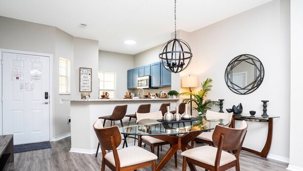 A modern kitchen with blue cabinets, a central island, and a dining area with a glass table and wooden chairs.