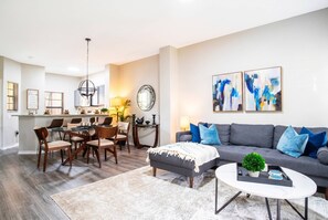 A modern living room with a grey sofa, a coffee table, and a dining area with a chandelier.