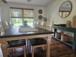 A dining room with a wooden table, chairs, a rug, a potted plant, a mirror, and decorative plates. - The Monarch - Private Setting, Heated Pool, 6 Bedroom, New Build. 6 min to CDP (Fly Creek)