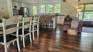 A modern kitchen with white cabinets, a dining area with wooden chairs, and a living room with a brown sofa. - The Monarch - Private Setting, Heated Pool,  6 Bedroom, New Build. 6 min to CDP (Fly Creek)