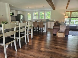 A modern kitchen with white cabinets, a dining area with wooden chairs, and a living room with a brown sofa. - The Monarch - Private Setting, Heated Pool, 6 Bedroom, New Build. 6 min to CDP (Fly Creek)