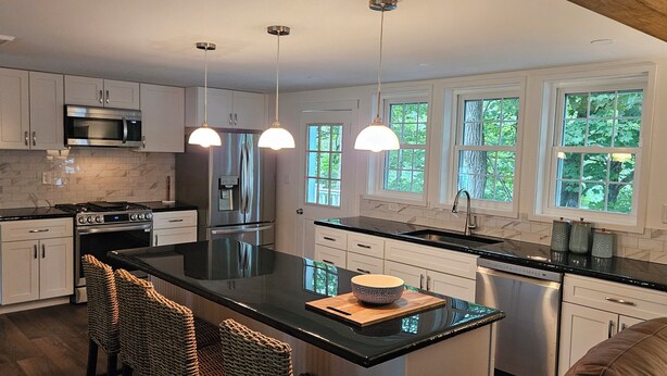 A modern kitchen with white cabinets, stainless steel appliances, a black countertop, and a large island with seating. - The Monarch - Private Setting, Heated Pool,  6 Bedroom, New Build. 6 min to CDP (Fly Creek)