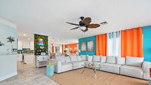 A modern living room with a sectional sofa, a glass coffee table, and a ceiling fan. - Anna Maria Island of Palms - HotTub,Pool,Poker,Games and more (ANNA MARIA)