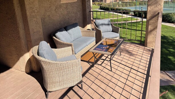 A covered patio area with wicker furniture, including a sofa and chairs, and a glass-top table.