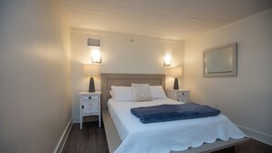 A bedroom with a bed, two bedside tables, a nightstand, a mirror, and a wall-mounted heater.