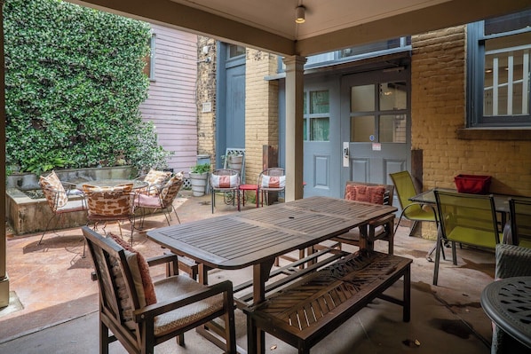 An outdoor patio with a wooden table and chairs, surrounded by brick walls and a large window.