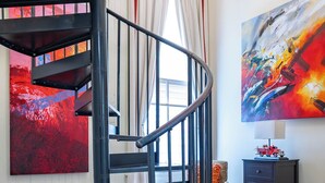 Un escalier en colimaçon dans une pièce où se trouvent une grande peinture abstraite, une voiture jouet ancienne et un fauteuil classique.