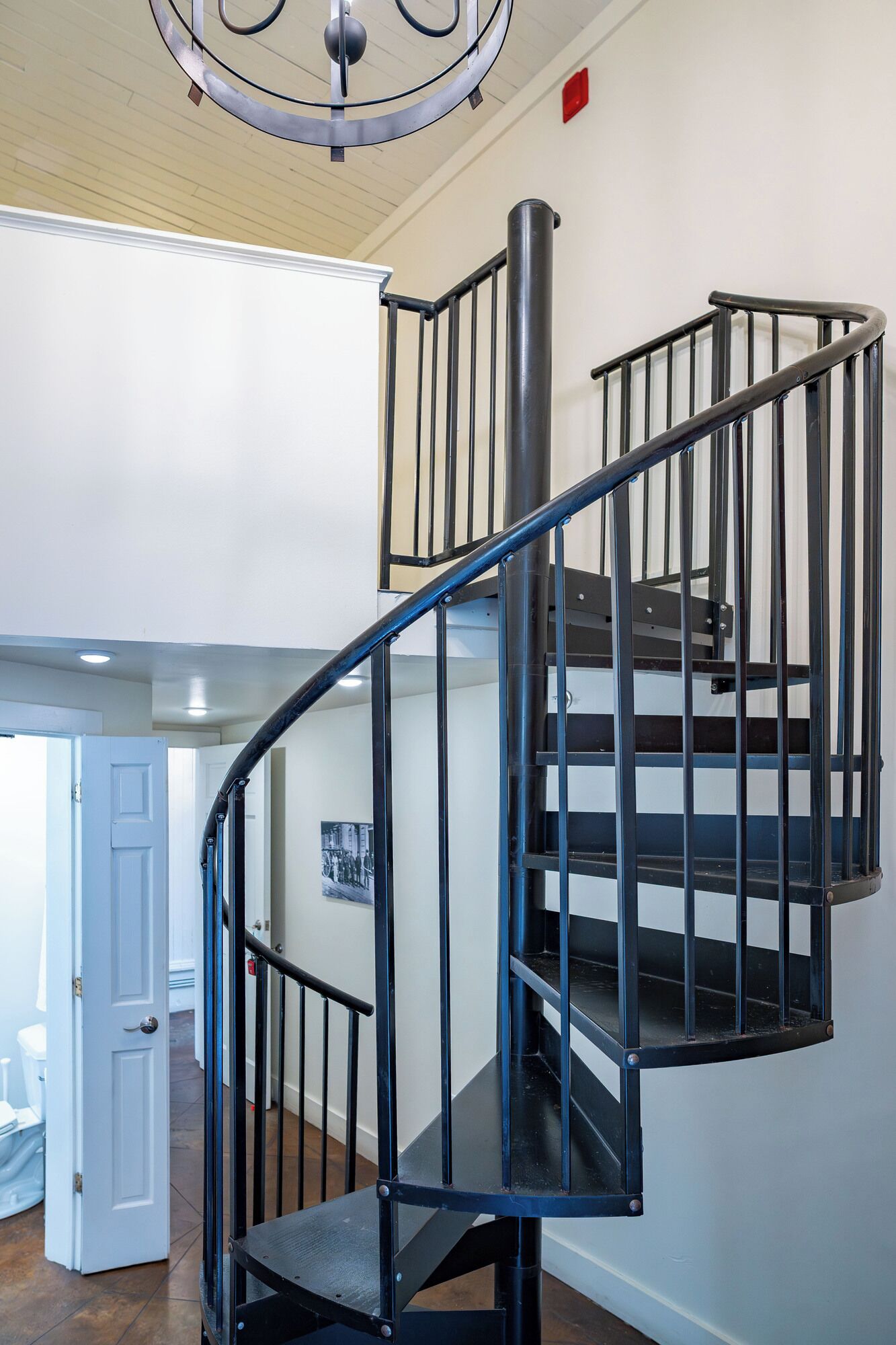 Una escalera en espiral con barandillas negras y un pasamanos metálico, que conduce a un piso superior.