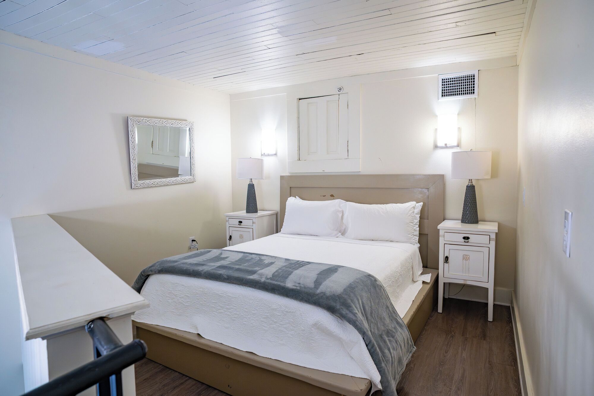 Een slaapkamer met een bed, nachtkastjes, een spiegel en een raam.