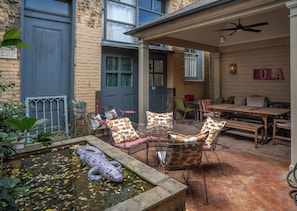 Une terrasse avec des meubles d’extérieur, un bassin décoratif et un bâtiment avec une porte bleue et une enseigne indiquant « SORTIE ».