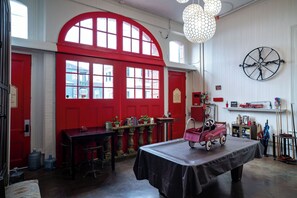 A room with a red door, a round table with a fire truck toy, and a wall-mounted bicycle wheel. - Engine 24 Firehouse Room 3 (New Orleans)
