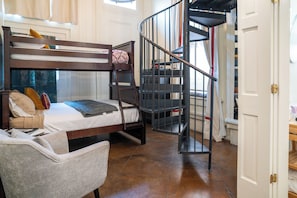A bunk bed with a ladder, a chair, a spiral staircase, and a door.