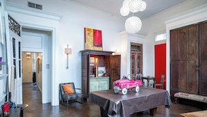 A room with a wooden table, a chair, a lamp, and a red door.