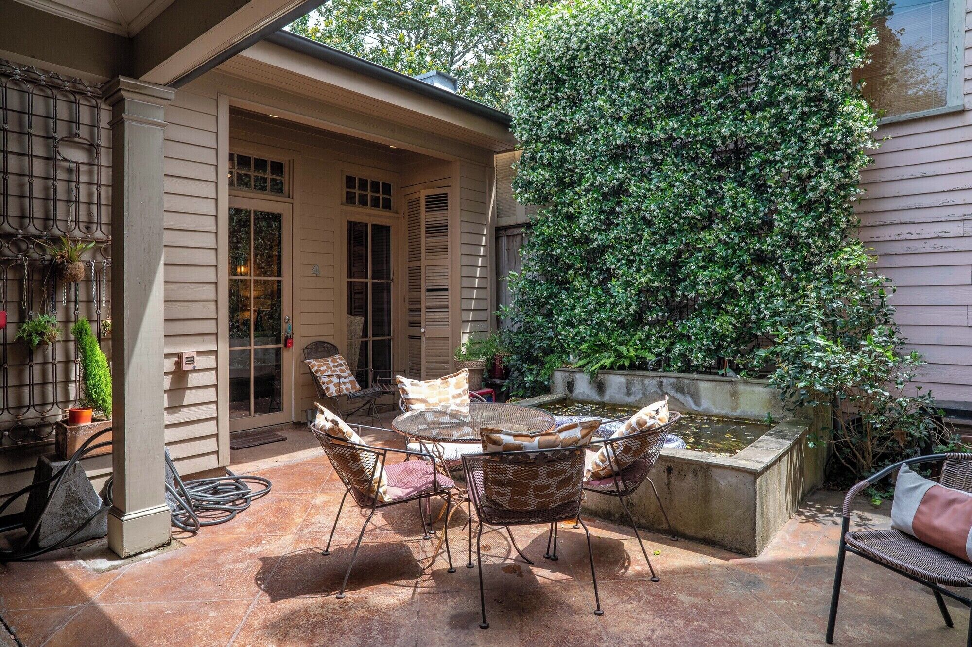 A patio with a round table and chairs, a small water feature, and a wall covered in climbing plants.