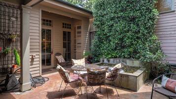 A patio with a round table and chairs, a small water feature, and a wall covered in climbing plants.