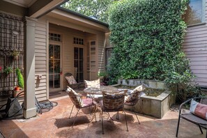 Une terrasse avec une table ronde et des chaises, une petite fontaine et un mur recouvert de plantes grimpantes.