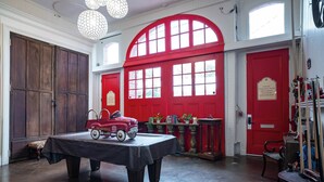 Una habitación con una mesa, un camión de bomberos antiguo de juguete, puertas rojas y una estantería.
