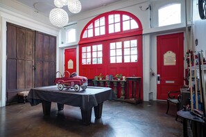 Une pièce avec une table, un camion de pompiers jouet d’époque, des portes rouges et une bibliothèque.
