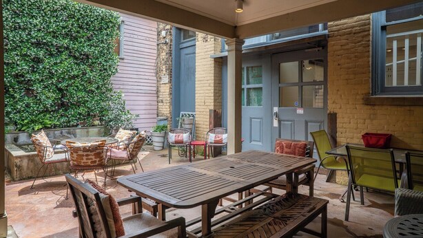 Un patio al aire libre con una mesa y sillas de madera, rodeado de paredes de ladrillo y un ventanal grande.