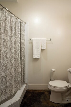 A bathroom with a shower curtain, a towel rack with two towels, a toilet, and a tiled floor. - Engine 24 Firehouse Courtyard Room 5 (New Orleans)
